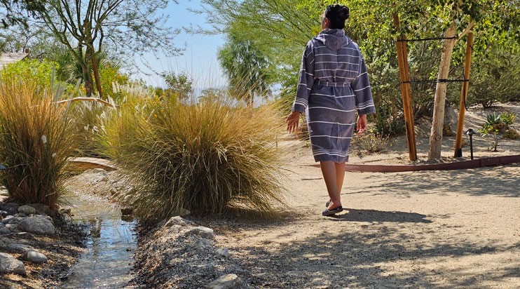 Woman strolling through the oasis alongside a stream and wispy grasses