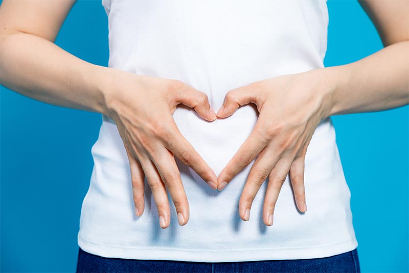 Detail of a woman making a heart symbol over her abdomen.